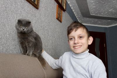 Boy with a gray cat sitting on the couch and smiling