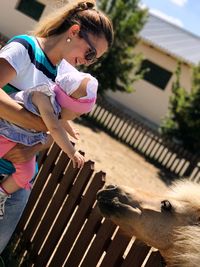 Baby girl reaching for horse while being carried by mother