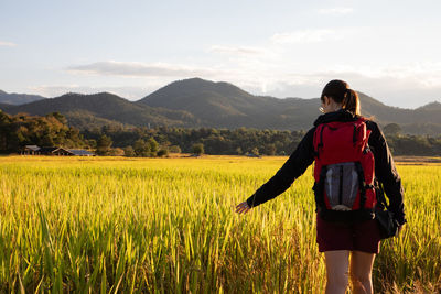 Rear view of woman walking at rice paddy against sky