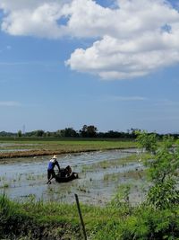 Men sitting on field by lake against sky