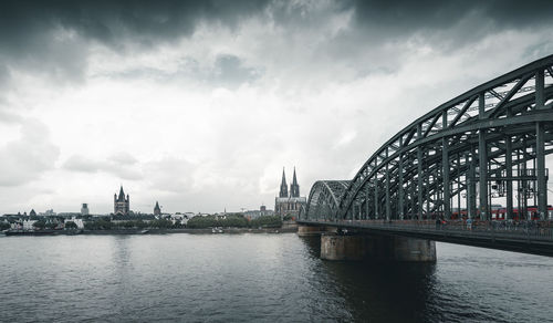 Bridge over river by buildings against sky