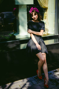 Beautiful young woman in black dress sitting on window