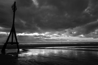 Silhouette pole at beach against cloudy sky