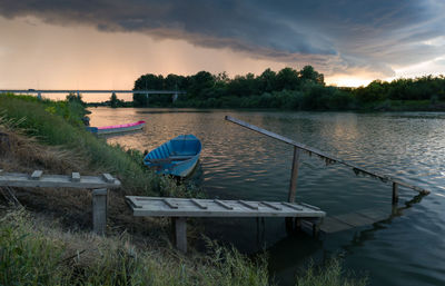 Empty chairs by lake against sky during sunset