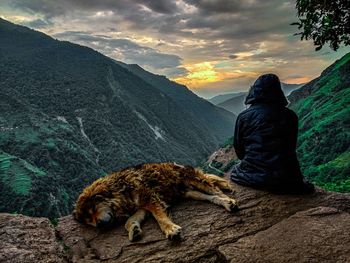 Rear view of man sitting on rock against sky
