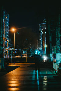 Illuminated street by buildings against sky at night