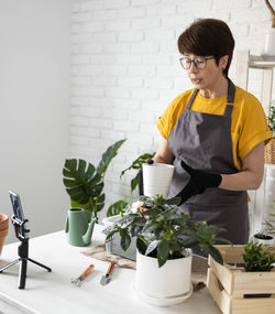 Side view of woman holding potted plant against white background