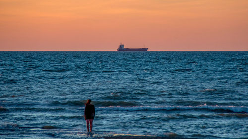 Rear view of silhouette man standing on beach against clear sky