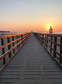 Pier at beach against clear sky during sunset