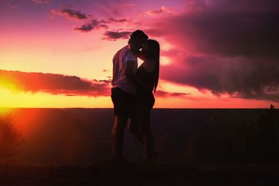 Silhouette romantic couple standing against sky during sunset