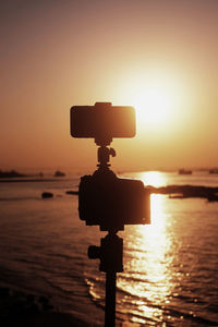 Silhouette information sign on sea against orange sky