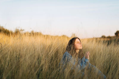 Young woman with arms raised on field against sky