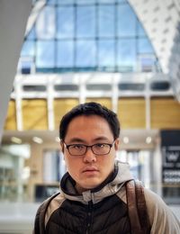 Portrait of young man in eyeglasses against architectural features inside mall.