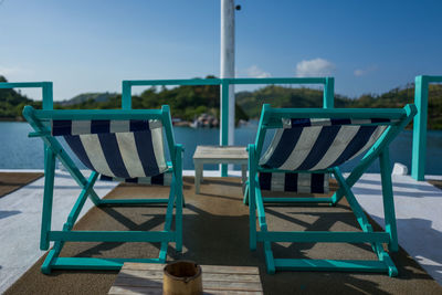 Empty chairs and tables at beach against blue sky