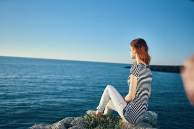 Woman sitting by sea against clear sky