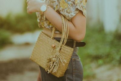 Midsection of woman holding wicker bag while standing outdoors