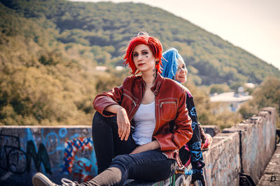 Portrait of young woman sitting on railing against mountain