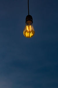Low angle view of illuminated light bulb against blue sky