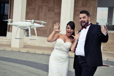 Shocked bride and groom looking at drone against building