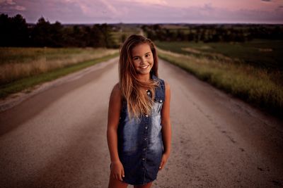 Portrait of girl standing on road at sunset