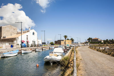 Rowboats moored in canal by road against sky