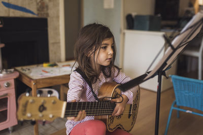 6 yr old girl with dark hair practicing guitar lesson in playroom