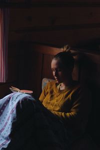 Woman reading book on bed in wooden cottage