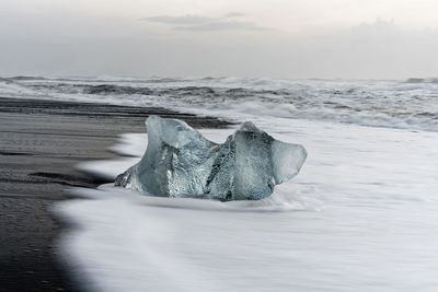 Ice blocks in blue and dark shades on a black beach with strong surf, iceland, jökulsarlon
