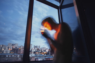 Shirtless man igniting cigarette by window at home