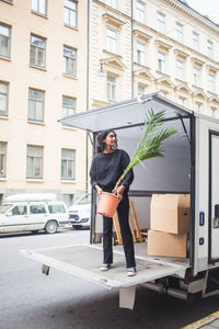 Female mover unloading potted plant from truck on street in city