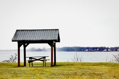 Lifeguard hut on field by lake against sky