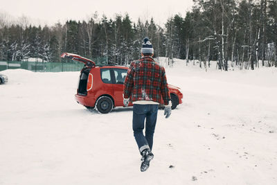 Rear view of man walking towards red car on snow covered landscape