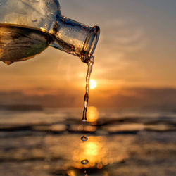 Close-up of water drop on sea against sky during sunset