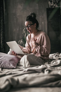 Woman using mobile phone while sitting on bed