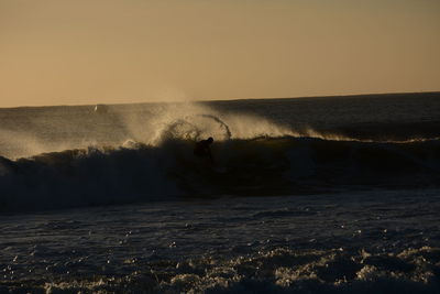 Man surfing on sea against clear sky during sunset