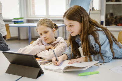 Curious schoolgirls doing e-learning through tablet pc sitting at desk in classroom