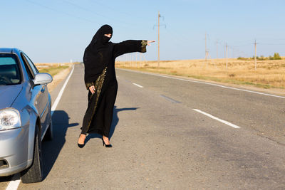 Full length of woman wearing burka standing on road against sky