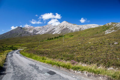 Road leading towards mountains against blue sky