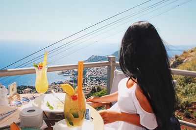 Rear view of woman sitting on table by sea against sky