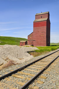 Railroad tracks by house on field against sky