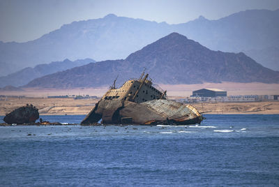 Shipwreck in sea against mountains