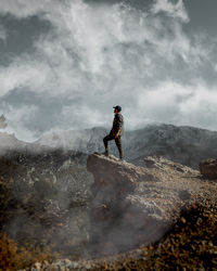 A person standing on the edge of a cliff with sky, clouds and mountains in the background.