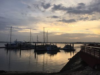 Boats moored at harbor against sky during sunset