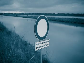 Information sign by lake against sky