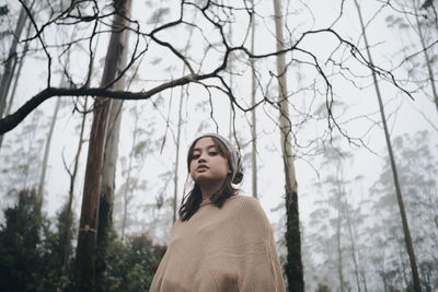 Young woman standing by bare trees during winter