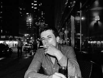 Portrait of man smoking at sidewalk cafe in city during night