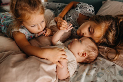 Two girls touching baby sibling and cuddling in bed together
