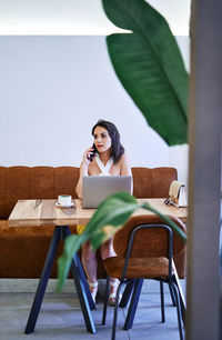 Female entrepreneur discussing business project on mobile phone while using netbook and working remotely at table in cafe