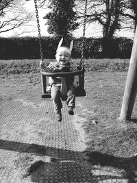 Cheerful toddler wearing headdress swinging on swing at playground