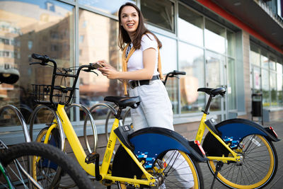 Smiling woman looking away while renting bicycle in city